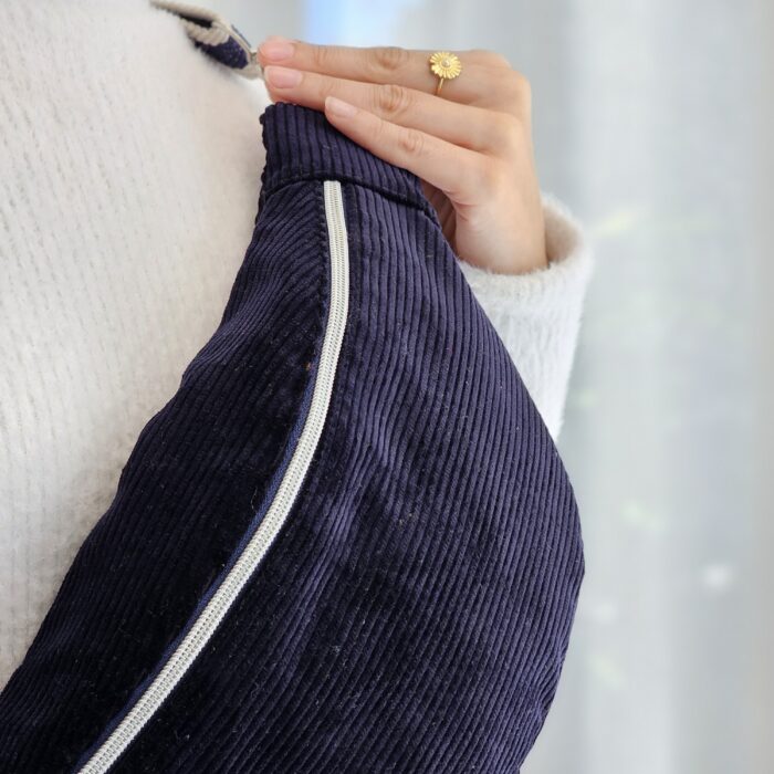 sac-banane-velours-bleu-marine.jpg Détail d’un sac banane en velours côtelé bleu marine avec fermeture éclair blanche porté à l’épaule