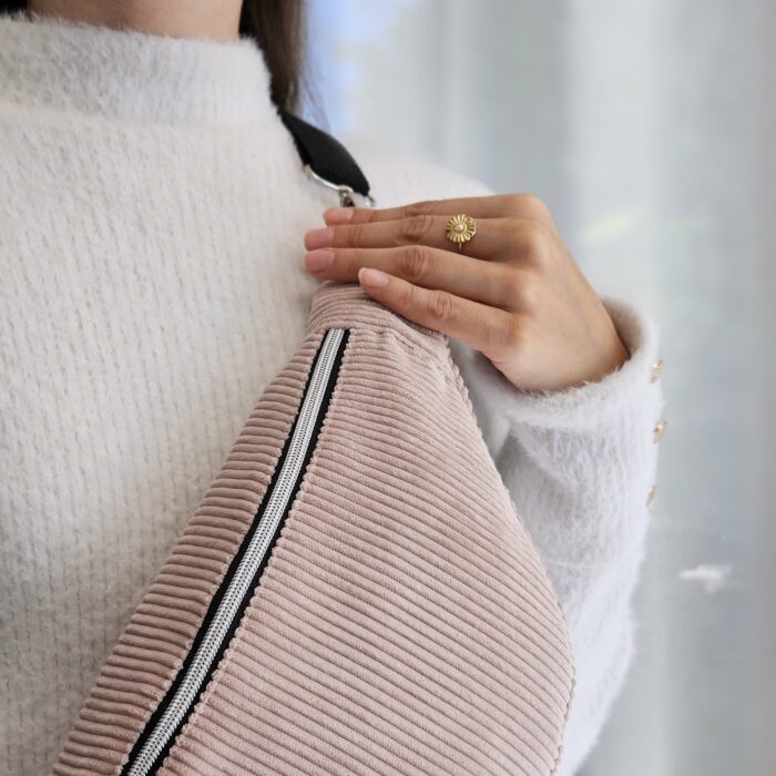 sac-banane-velours-rose-poudre-personnalise.jpg Sac banane en velours côtelé rose poudré porté avec un pull blanc, personnalisable par broderie
