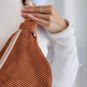 Détail d’un sac banane en velours côtelé terracotta avec fermeture éclair beige porté à l’épaule