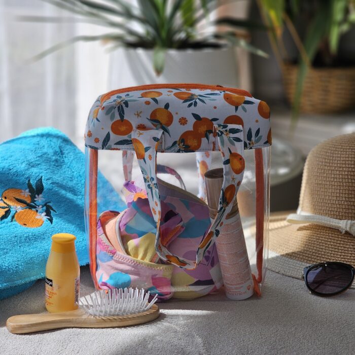 sac-maillot-transparent-motif-oranges-plage.jpg Sac à maillot de bain transparent motif oranges rempli d’accessoires de plage dans une ambiance estivale